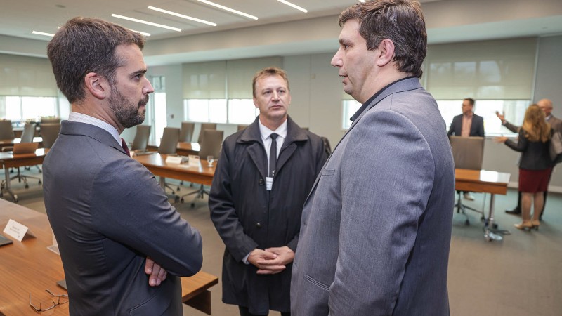 Três homens conversam com sala de reuniões ao fundo