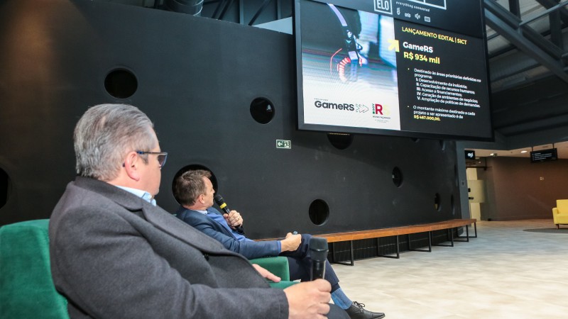 Dois homens olhando para uma tela que exibe informações sobre o edital GameRS