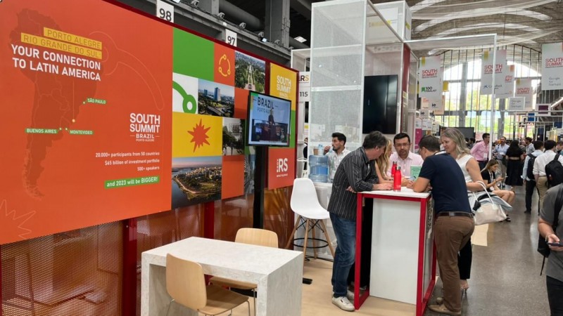 Estande com fundo laranja, verde e amarelo com imagens de Porto Alegre e números do South Summit Brasil