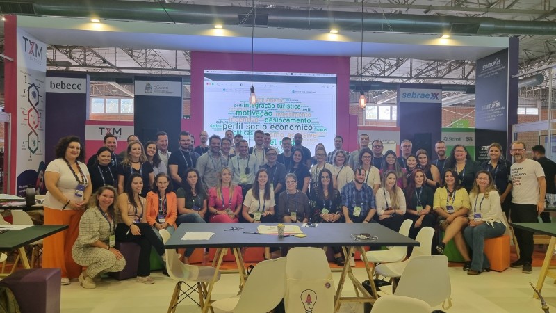 Cerca de 50 pessoas posam para foto em frente a um painel com nuvem de palavras.