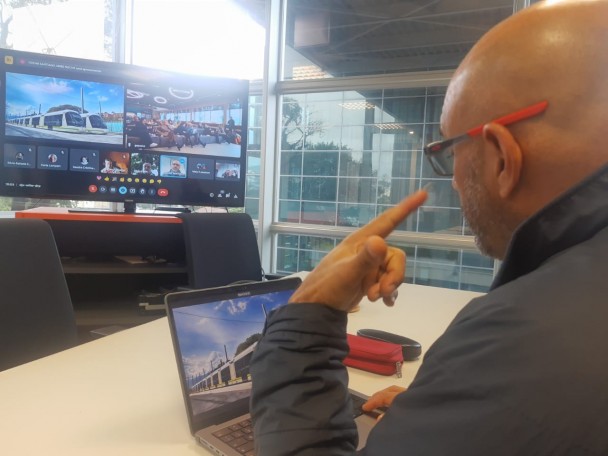 Homem fala em frente a uma tela de computador