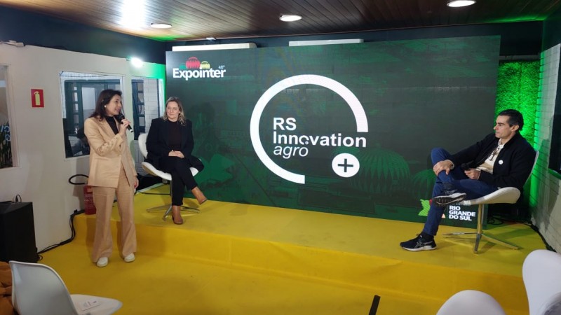Três pessoas em cima de um palco, com um telão ao fundo