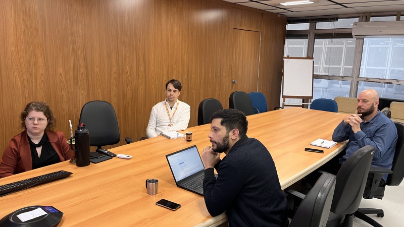 Quatro pessoas sentadas em volta da mesa, em reunião. 