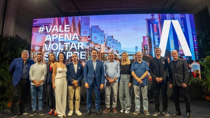 Autoridades, homens e mulheres, posicionados para foto no palco, &agrave; frente de um tel&atilde;o.