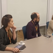 Duas pessoas, homem e mulher, posicionados em uma mesa de reunião