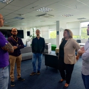 Cinco pessoas, posicionadas em círculo, conversam em um escritório.