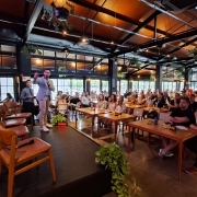 Homem num palco, com microfone na mão, fala para o público.