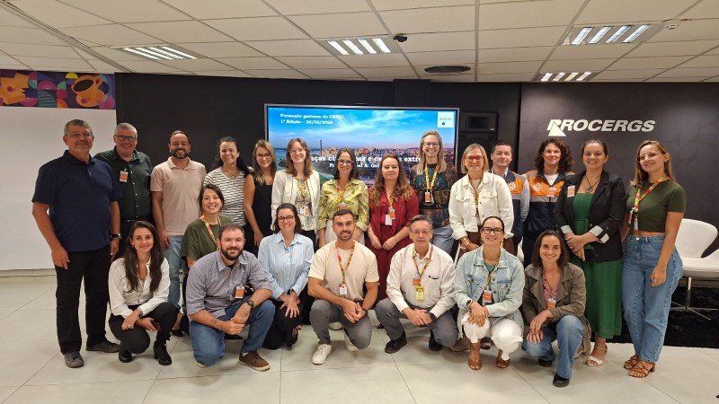 Homens e mulheres posam para foto, com um tel&atilde;o ao fundo.