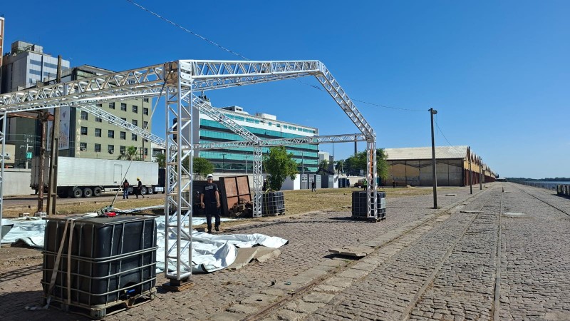 Estrutura met&aacute;lica aparece em primeiro plano, com pavilh&otilde;es amarelos ao fundo.
