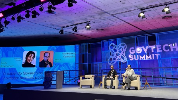 Painel do GovTech Summit 2026 em palco iluminado, com dois representantes da Sict debatendo pol&iacute;ticas p&uacute;blicas de inova&ccedil;&atilde;o